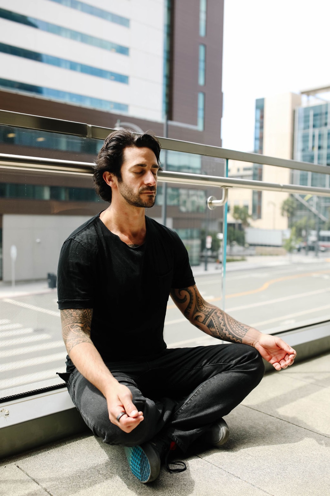 Peter cross-legged in meditation on an urban balcony, eyes closed.